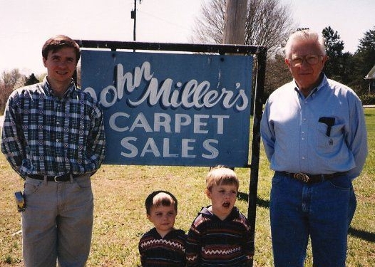 Mitch, Jonathan, Jordan and John Miller in front of the original John Miller's Carpet Sales sign in Englewood, Tennessee
